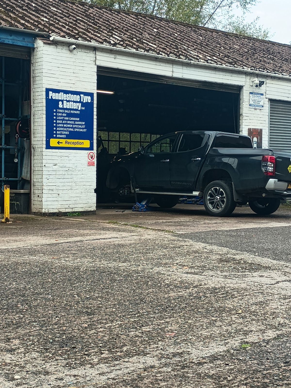The Pendlestone Tyre & Battery workshop at Fort Pendlestone, with a pickup raised in the open bay and the blue sign by the door